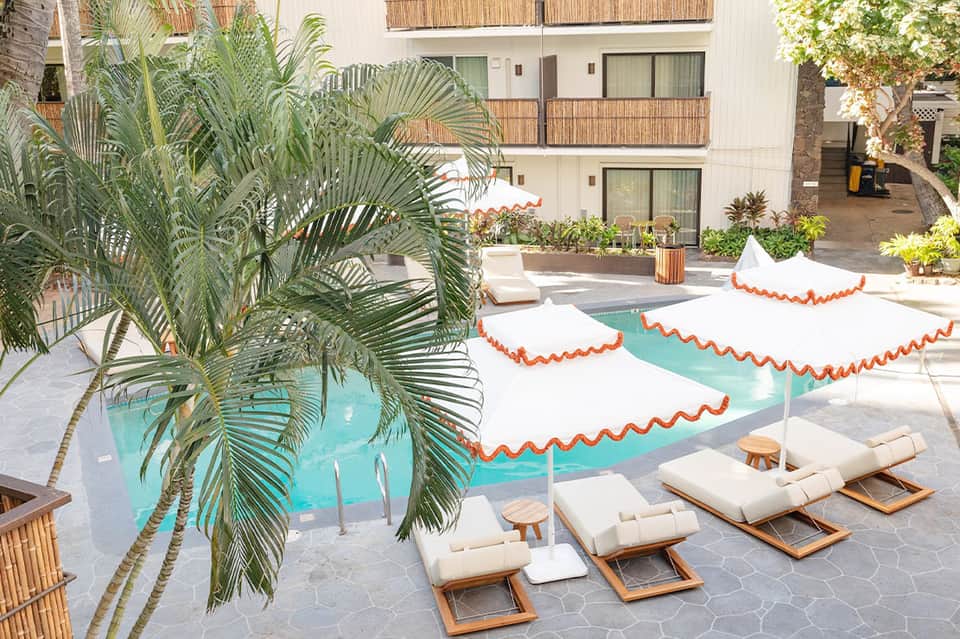 Resort pool area with turquoise water, white and orange scalloped umbrellas, lounge chairs, and palm tree