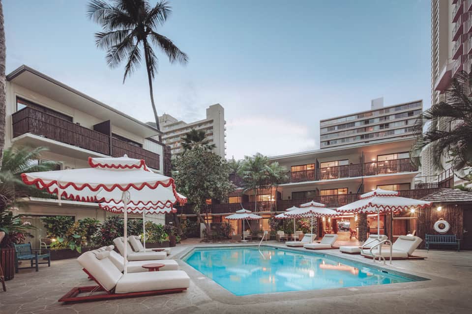 Resort pool with red and white striped umbrellas, loungers, and palm trees