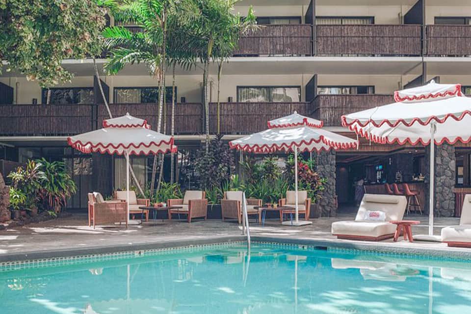 Resort pool area with red and white umbrellas, lounge chairs, and tropical landscaping