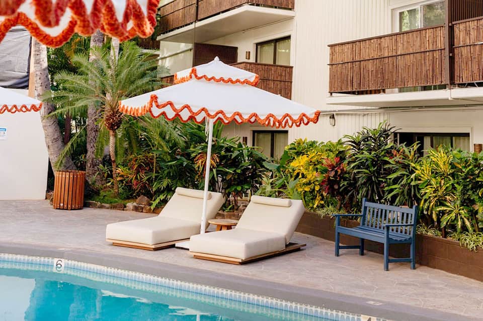Resort pool deck with white and orange striped umbrella, lounge chairs, and lush greenery