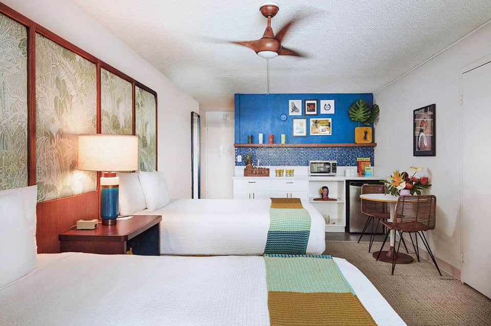 Colorful hotel guest room with two beds, kitchenette, blue accent wall, and modern furnishings
