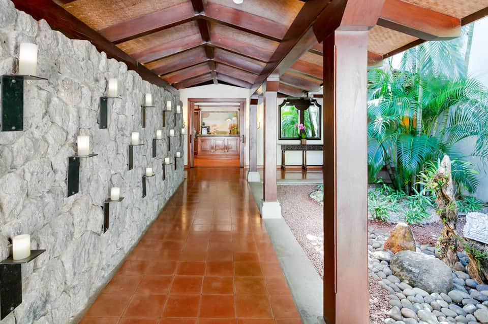 Covered walkway with stone walls, wooden beams, candle sconces, and tropical garden view