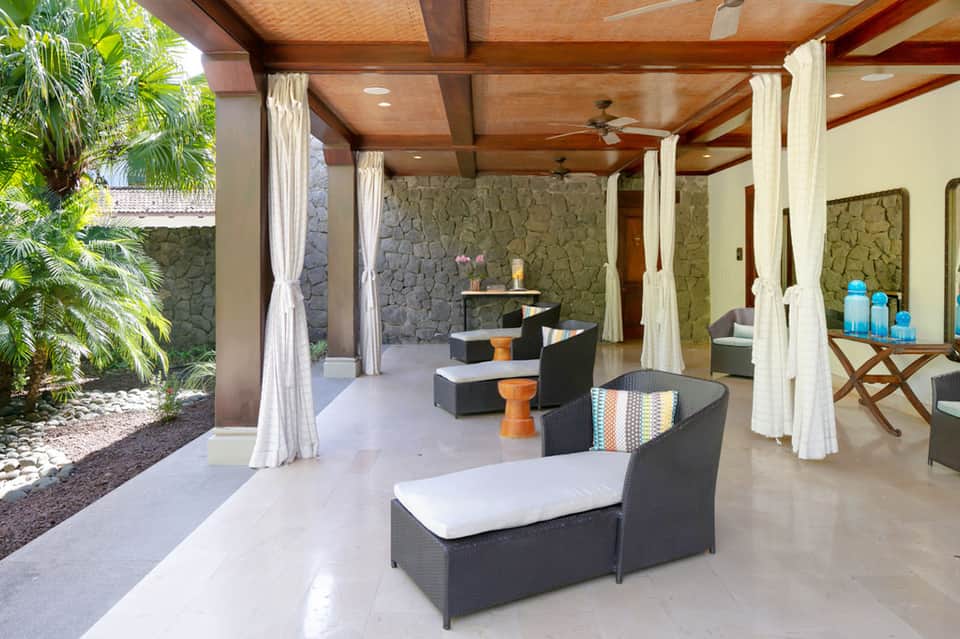 Outdoor spa cabana with white curtains, lounge chairs, and stone accent walls