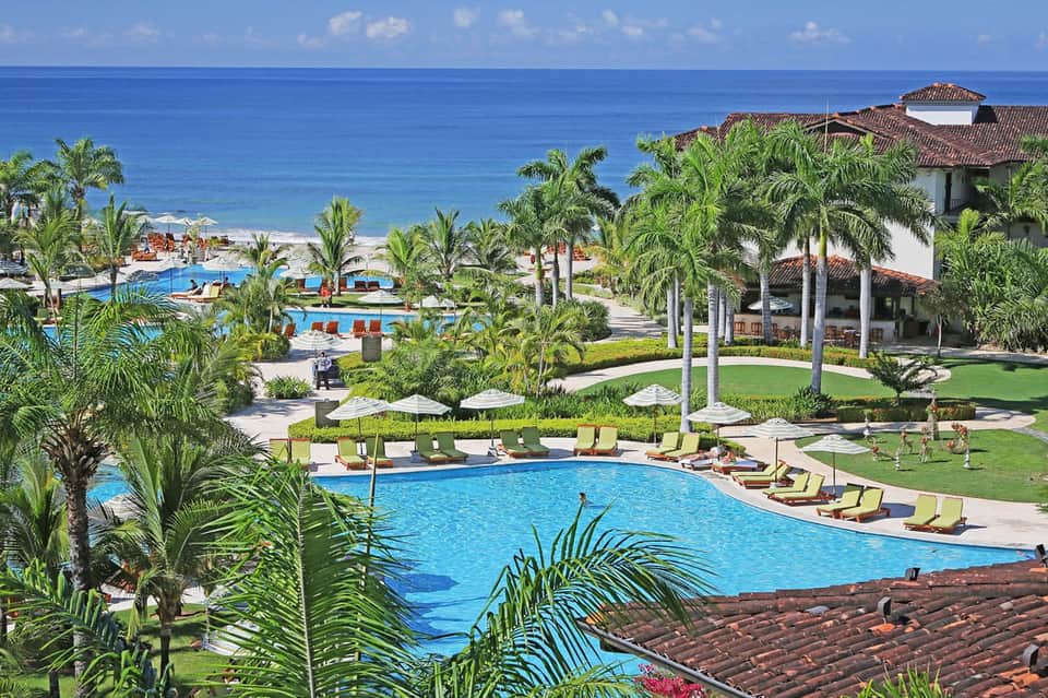 Beachfront resort with multiple pools, palm trees, and ocean horizon
