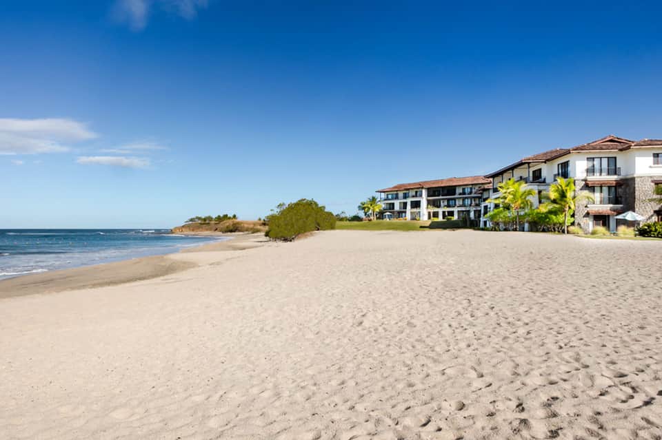 Beachfront property with sandy shore, residential buildings, and clear blue water