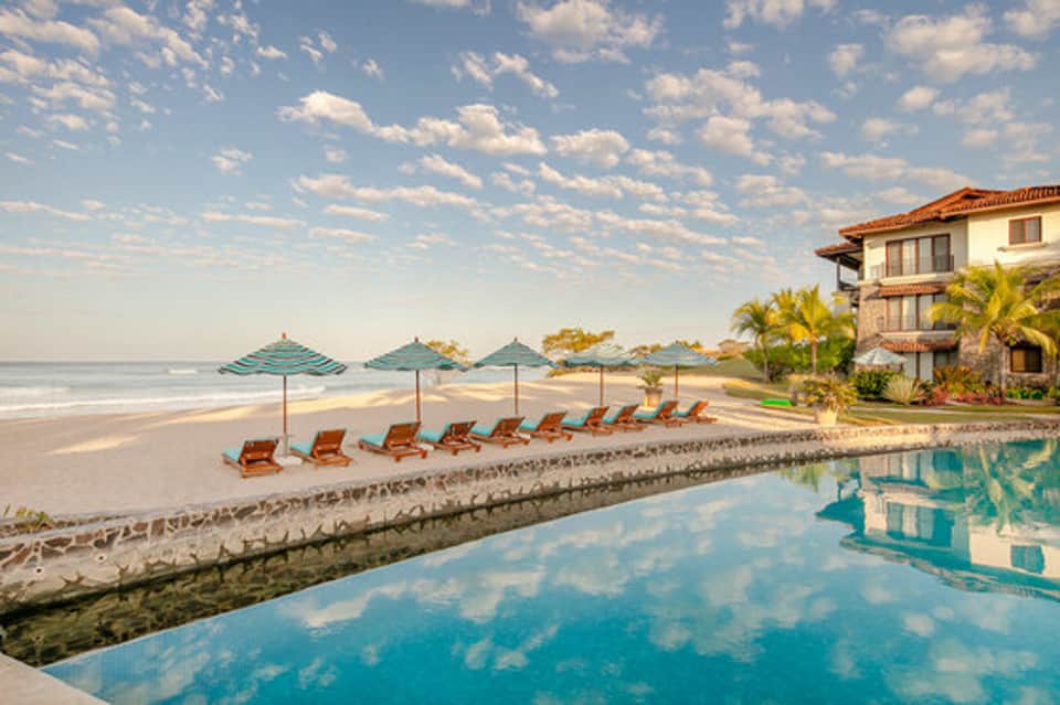 Beachfront resort with infinity pool, loungers, umbrellas, and ocean view at sunset