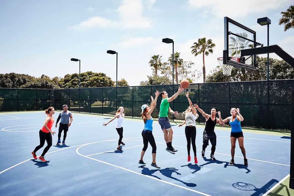 Group playing basketball on outdoor court with palm trees and modern lighting poles