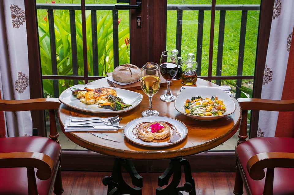 Plated dinner with wine glasses on balcony table overlooking green gardens