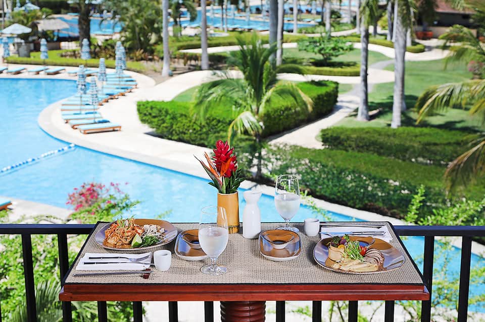 Outdoor dining table overlooking curved pool with white lounge chairs and green landscaping