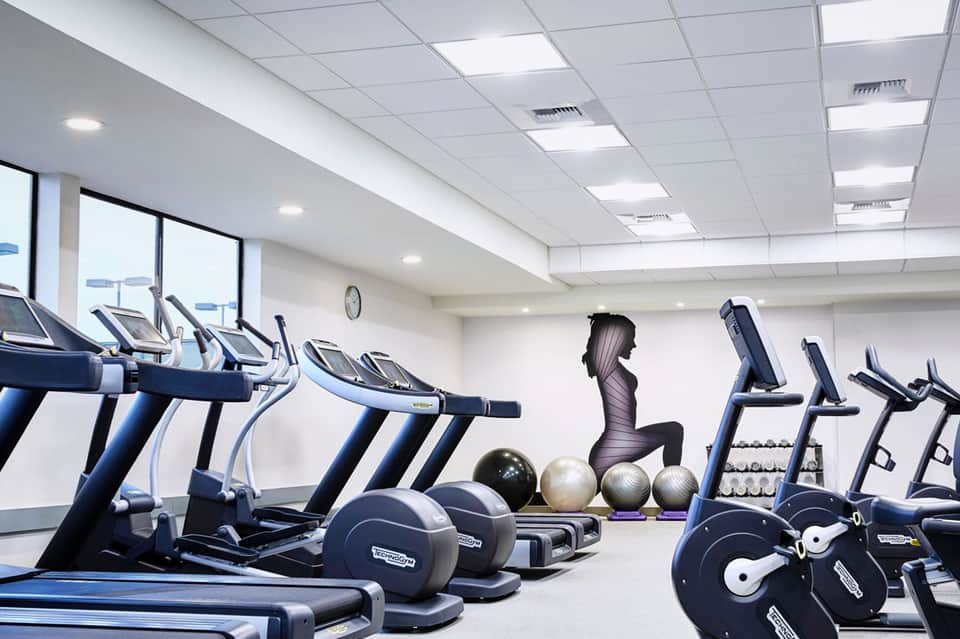 Modern fitness center with cardio equipment, exercise balls, and strength training machines under bright ceiling lights
