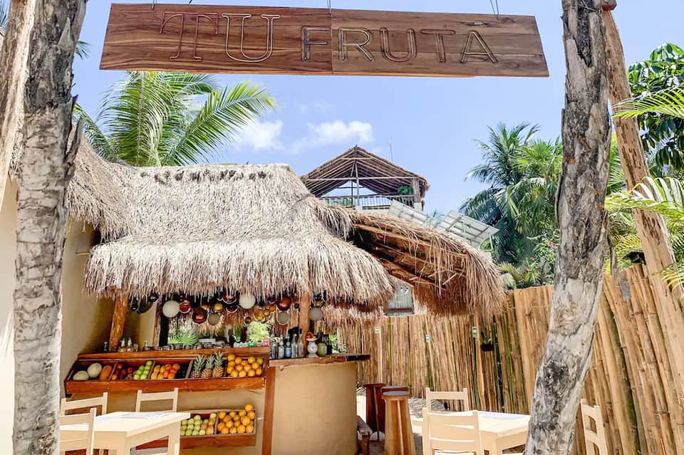 Thatched-roof 'Mi Fruta' tropical bar with fresh fruit display and palm trees