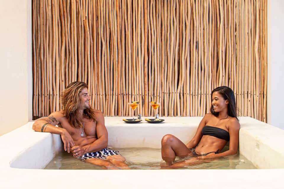 Couple relaxing in luxurious soaking tub with wooden wall backdrop and cocktails