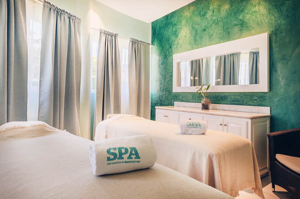 Spa massage room with twin treatment beds, green accent wall, and natural lighting