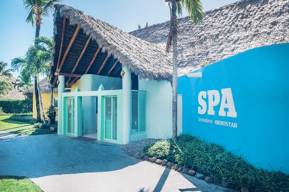 Blue spa building with thatched roof and turquoise shutters surrounded by palm trees