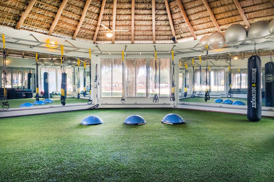 Modern fitness facility with suspended training equipment, mirrors, and thatched ceiling design