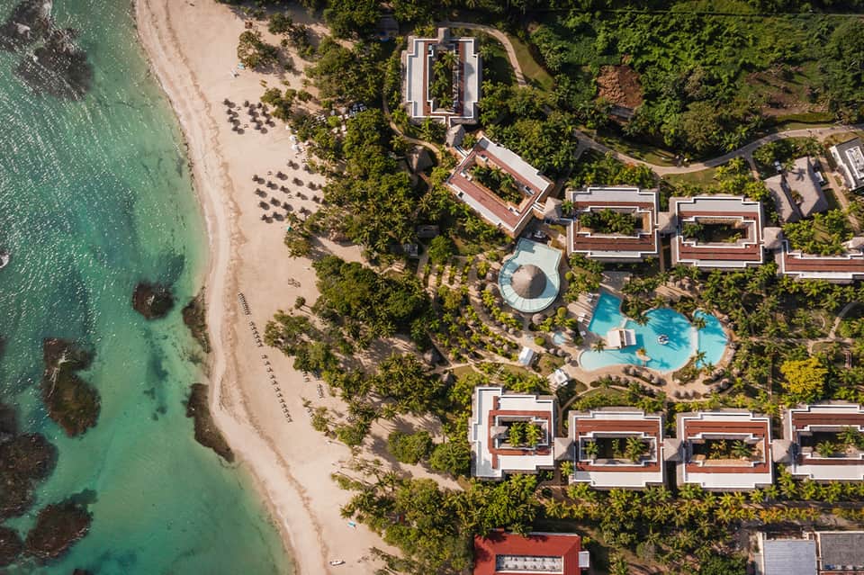 Aerial view of tropical resort nestled between lush vegetation and turquoise ocean with curved pool