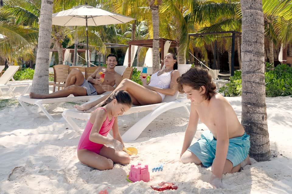Family enjoying beach with children playing in sand under palm trees and umbrellas