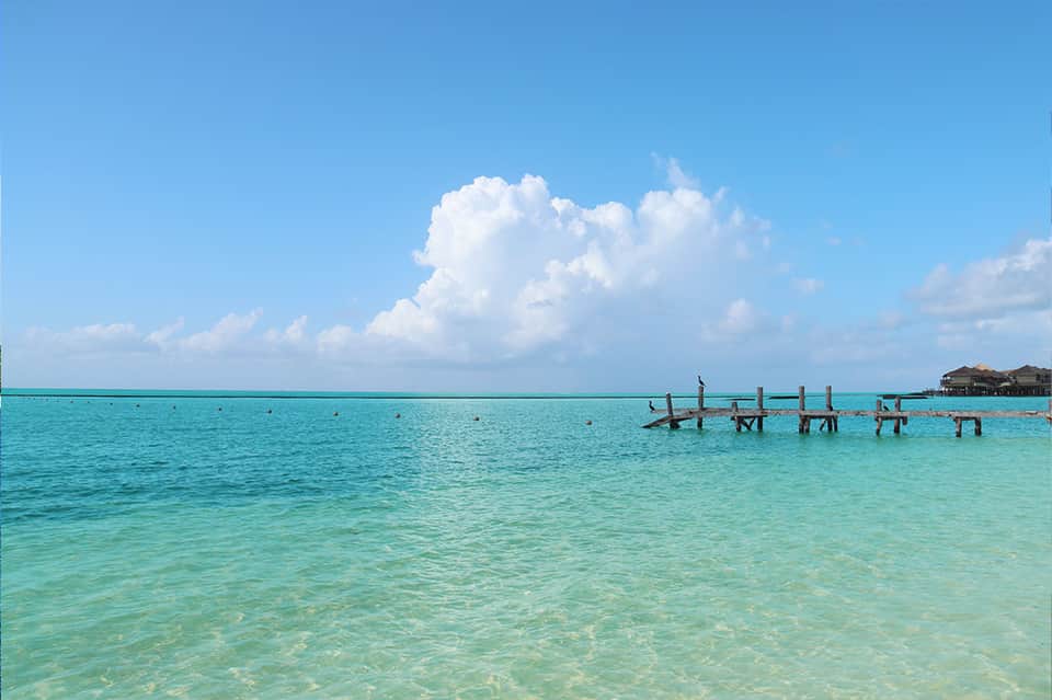 Turquoise tropical ocean with wooden pier and overwater bungalows under blue sky