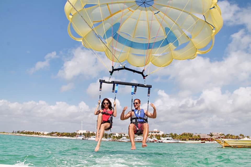 Two people parasailing over turquoise water with yellow parachute and tropical shoreline