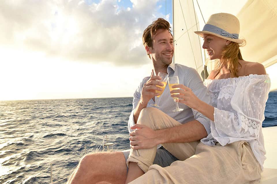 Couple toasting with champagne glasses on a sailboat at sunset overlooking ocean