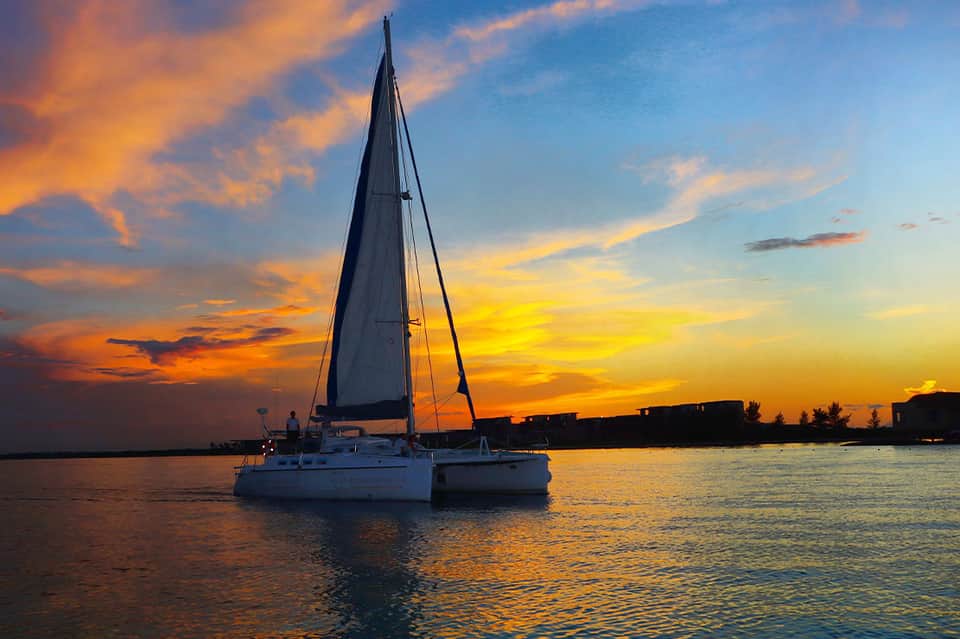 Sailboat anchored at sunset with golden sky reflecting on calm tropical water