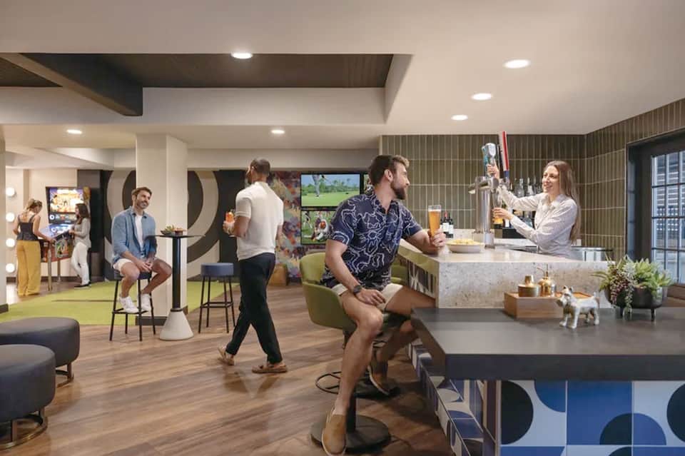 Contemporary hotel lounge with bar, fitness equipment, gaming area, and casual seating