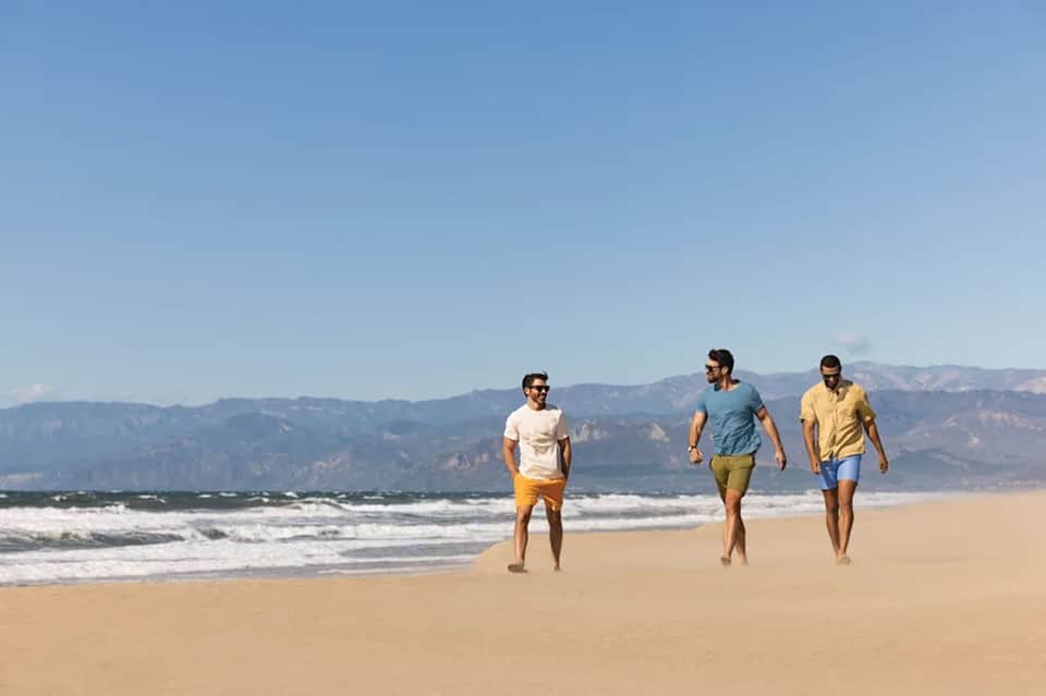 Three men jogging on beach with mountains in background and ocean waves