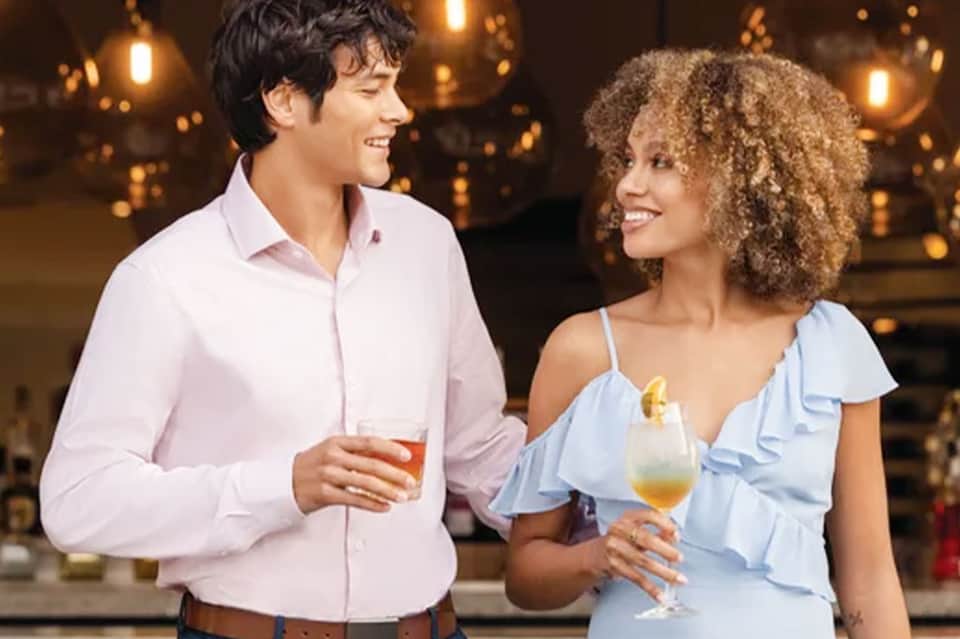 Couple enjoying cocktails at evening hotel bar with warm amber lighting and city skyline backdrop