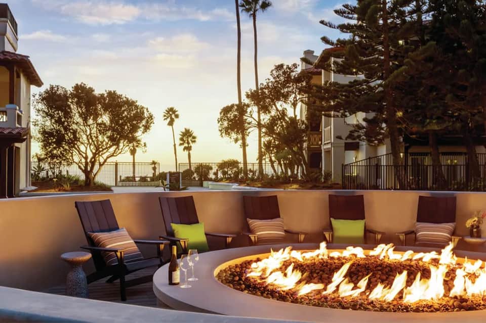 Coastal resort terrace with fire pit, Adirondack chairs, palm trees, and ocean overlook at golden hour