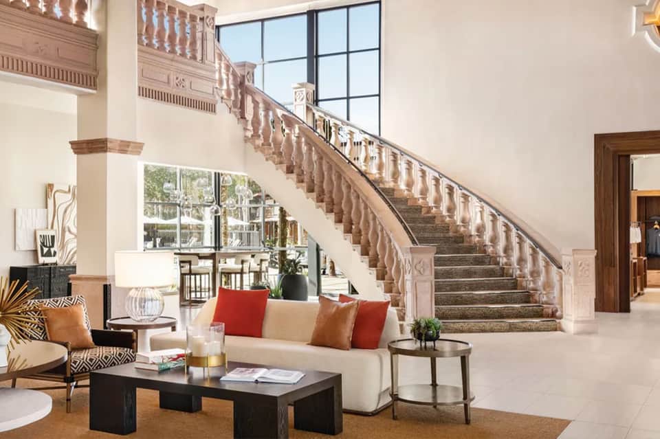 Grand hotel lobby with ornate staircase, modern furniture, and large windows