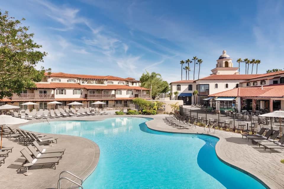 Resort courtyard with curved pool, loungers, Spanish colonial architecture and palm trees