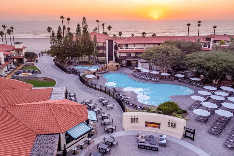 Sunset view of beachfront resort with multiple pools, red-tiled roofs, and palm trees