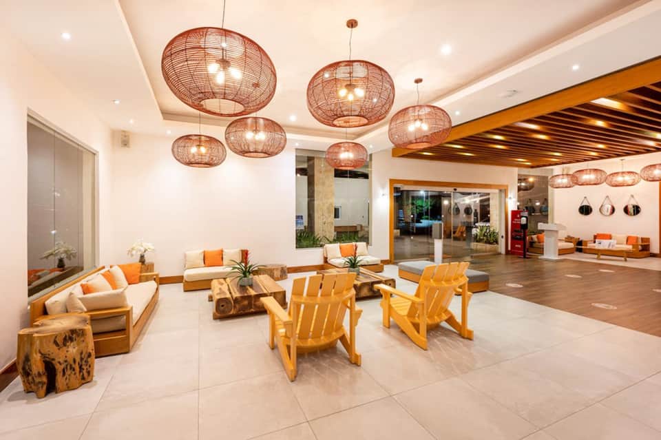 Modern hotel lobby with orange accents, woven pendant lights, and wooden furniture