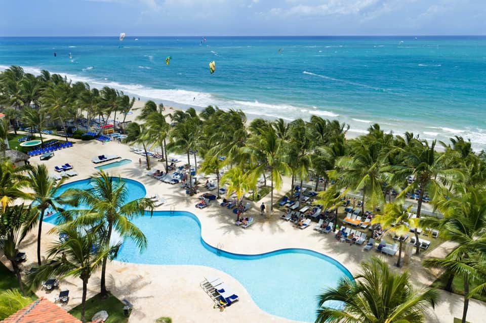 Aerial view of curved pool, beach, palm trees, and ocean with water sports activities