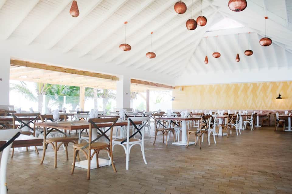 Bright dining pavilion with copper pendant lights, wooden chairs, and ocean views