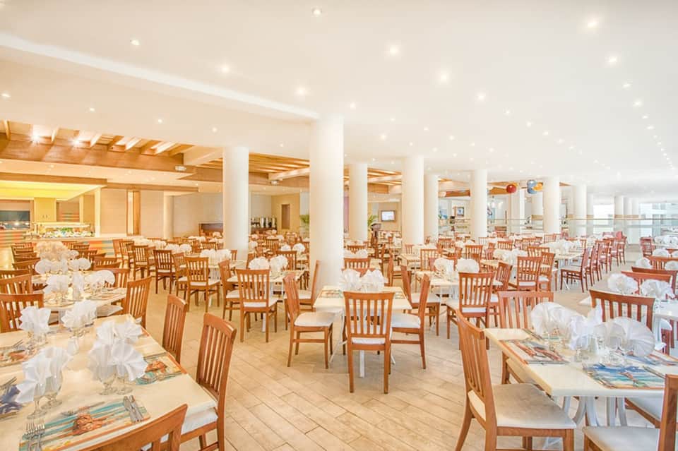 Spacious dining hall with wooden chairs, white linens, and ocean views