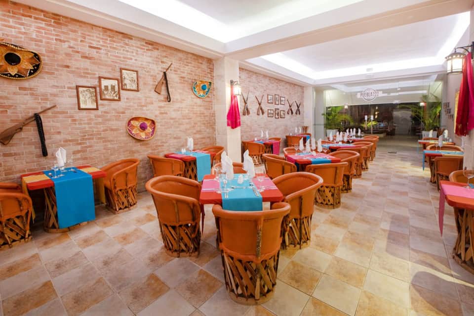Vibrant dining room with exposed brick walls, orange chairs, and colorful table runners for group events