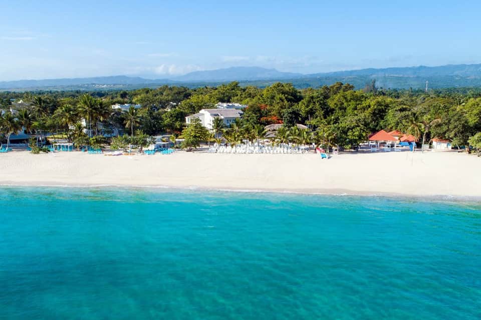 Aerial beach view with turquoise ocean, white sand, palm trees, and beachfront resort buildings
