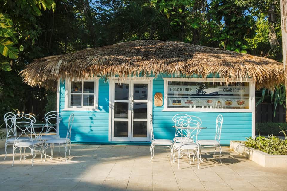 Beachside cigar lounge with turquoise walls, thatched roof, and white furniture