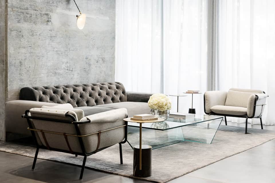 Contemporary living room with tufted sofa, modern chairs, glass coffee table, and concrete wall