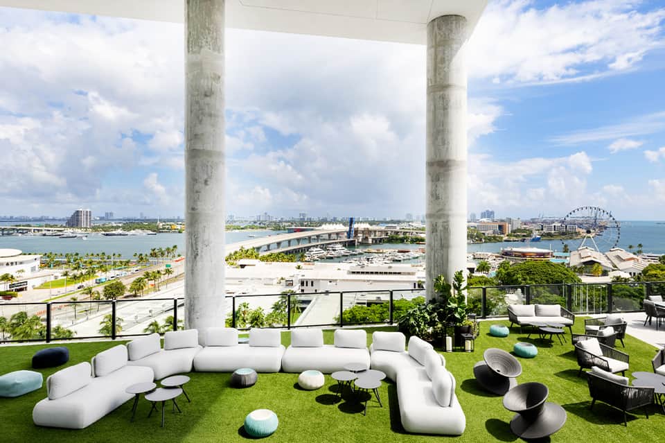 Modern lounge with curved white seating, colorful cushions, concrete pillars, and expansive water view