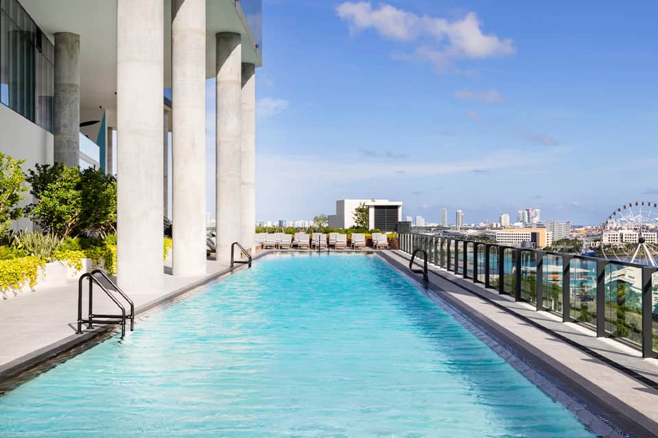 Rooftop infinity pool with city skyline views, modern concrete architecture, and lounge seating