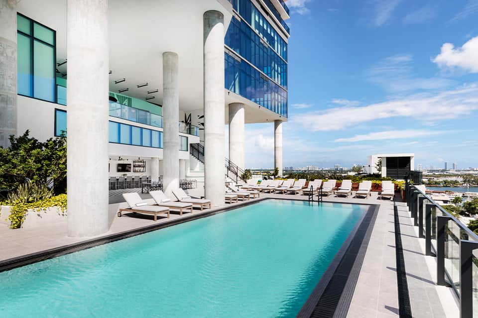 Contemporary rooftop pool with turquoise water, white loungers, and city waterfront views
