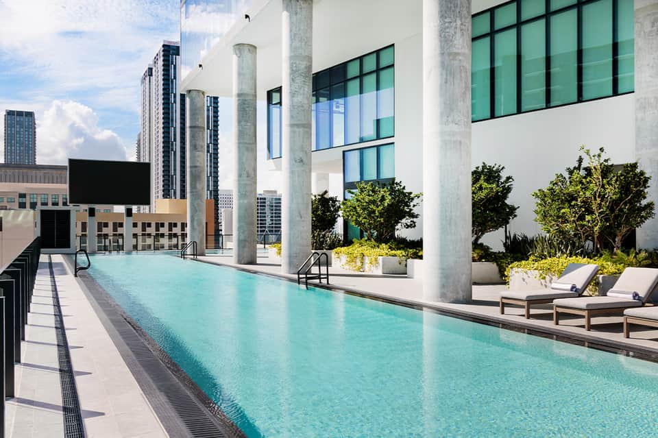 Rooftop infinity pool with city skyline views, lounge chairs, and modern architecture
