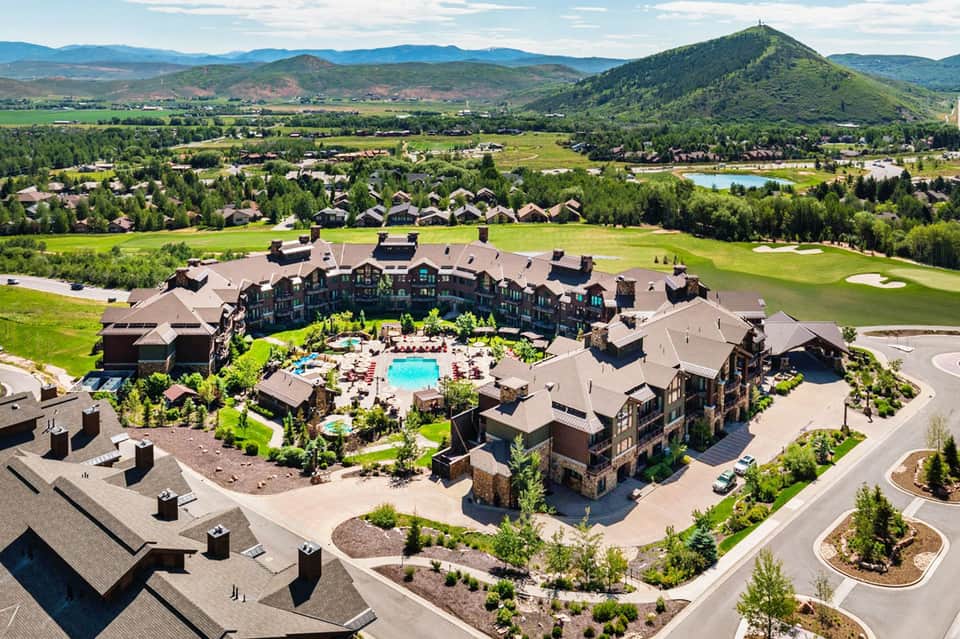 Luxury mountain resort with sprawling dark-roofed buildings, central pool, and scenic valley with mountains in background
