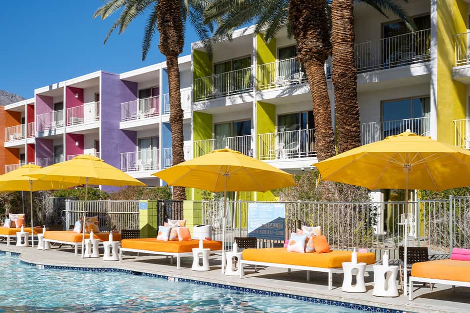 Colorful beachfront resort buildings with yellow umbrellas, orange loungers, and palm trees