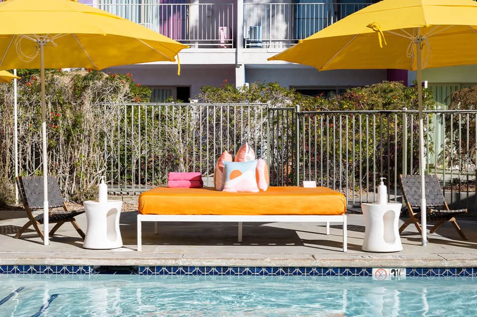 Poolside lounge with yellow umbrellas, colorful cushioned lounger, and tropical landscaping