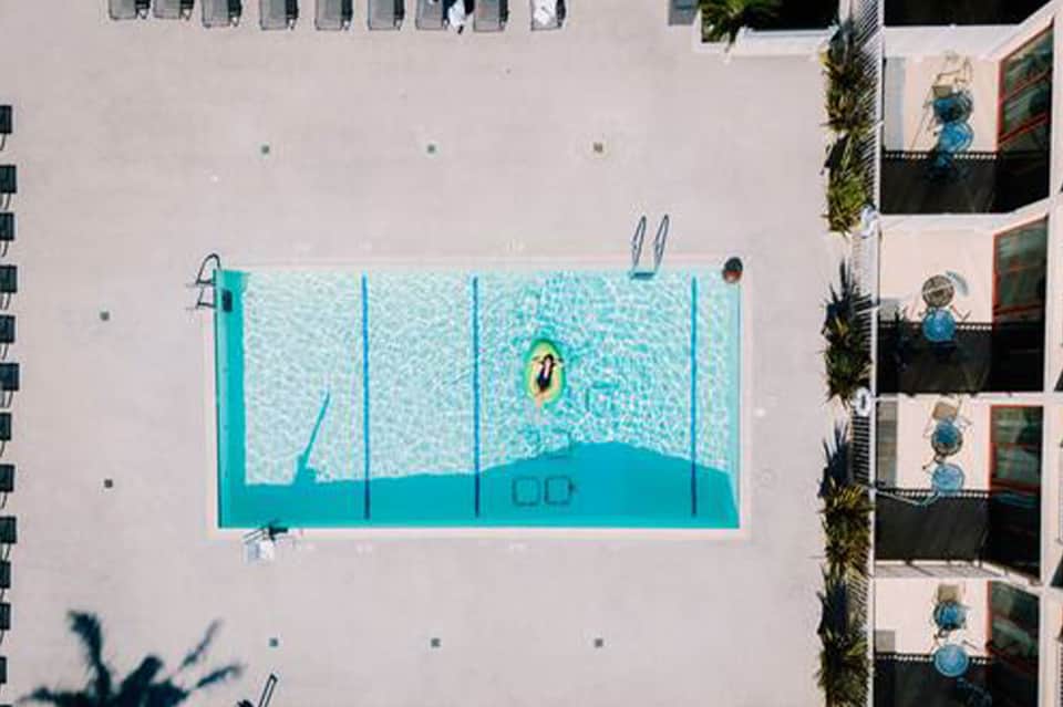 Overhead view of small turquoise swimming pool surrounded by white concrete deck near residential building