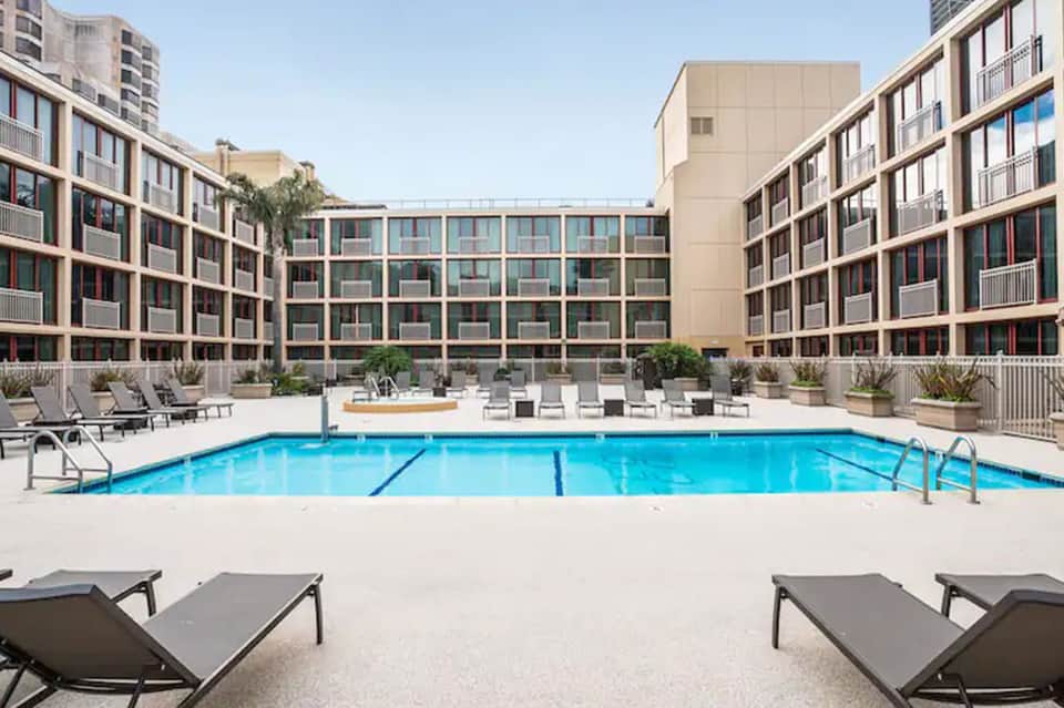 Modern resort courtyard with rectangular swimming pool, lounge chairs, and residential buildings