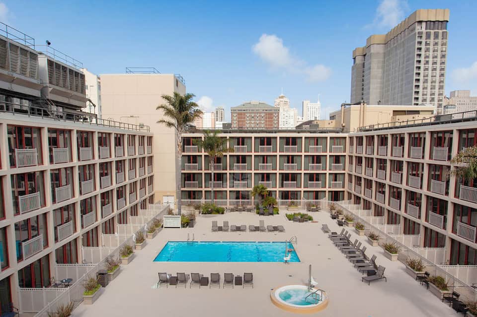 Aerial courtyard view of modern hotel with central pool, multiple room balconies, city skyline